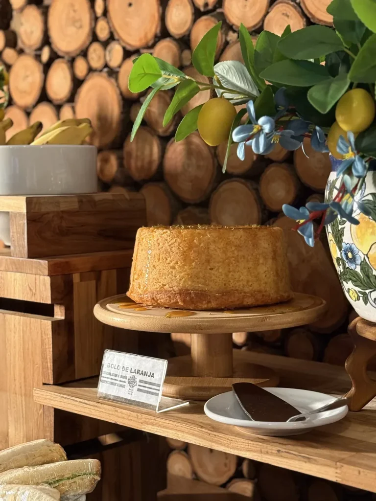 Bolo de laranja com calda, sobre suporte de madeira, ao lado do vaso de cerâmica com limões.
