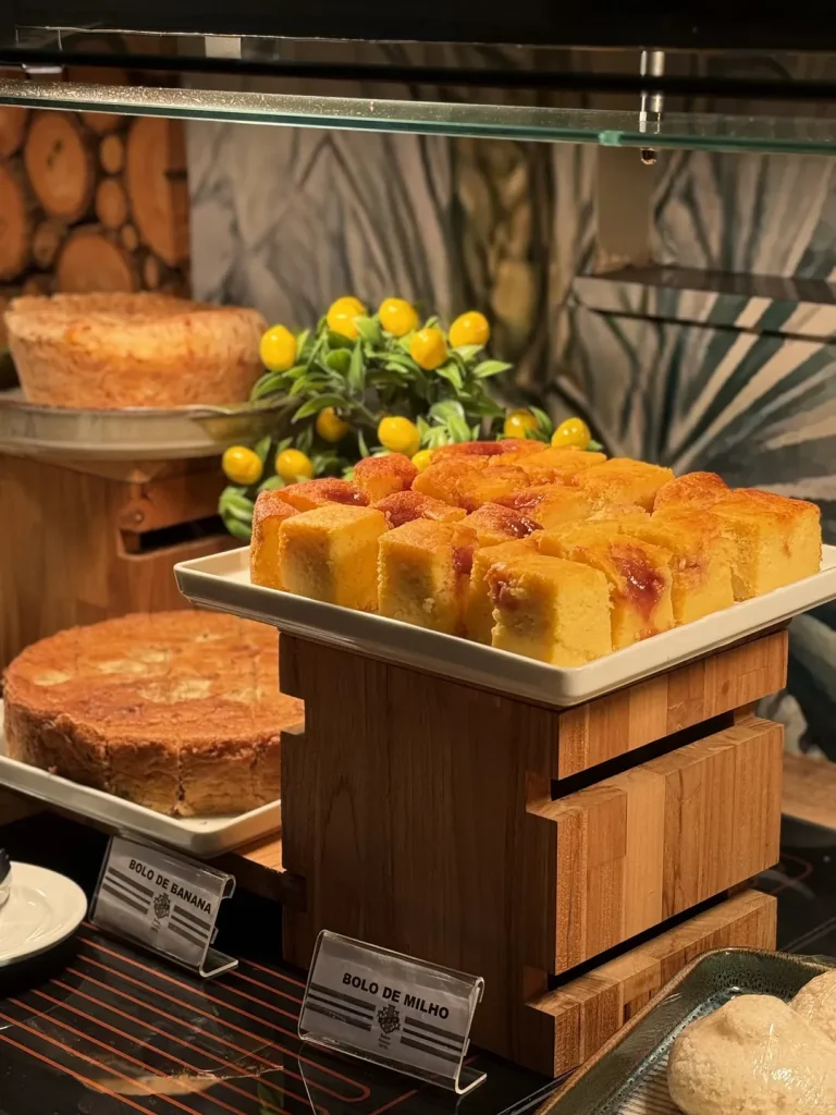 Bolo de milho em cubos servido em travessa branca sobre suporte de madeira.