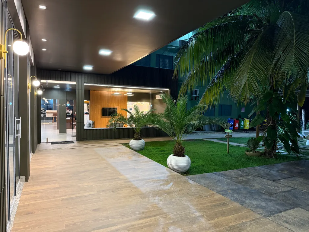 Passagem coberta do hotel ao anoitecer, com jardim de palmeiras iluminado ao lado