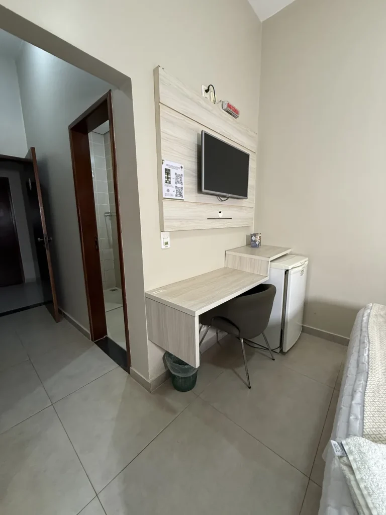 Bancada de trabalho com cadeira e frigobar, ao lado da porta do banheiro