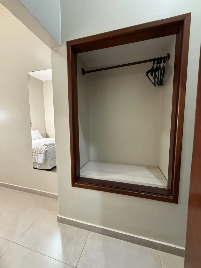 Armário embutido aberto com cabideiro, com a cama refletida no espelho ao lado