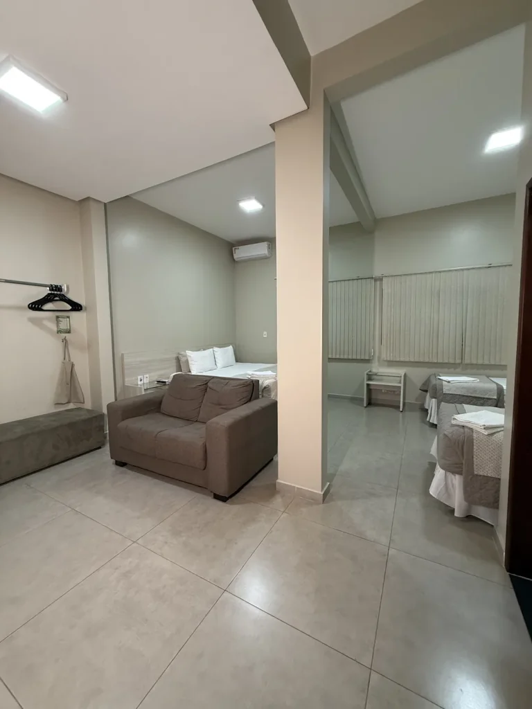 Sofá junto à coluna, com as camas da suíte ao fundo, no formato com duas camas de solteiro