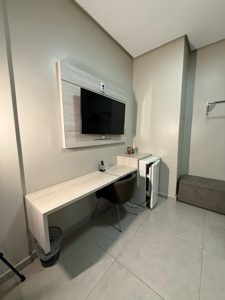 Bancada de trabalho com cadeira sob a TV no painel, ao lado do frigobar
