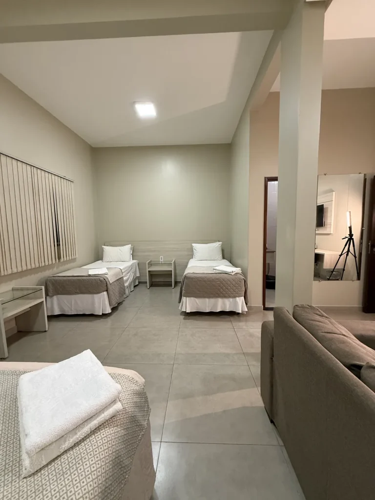 Duas camas de solteiro com criado-mudo entre elas, vistas a partir da cama queen