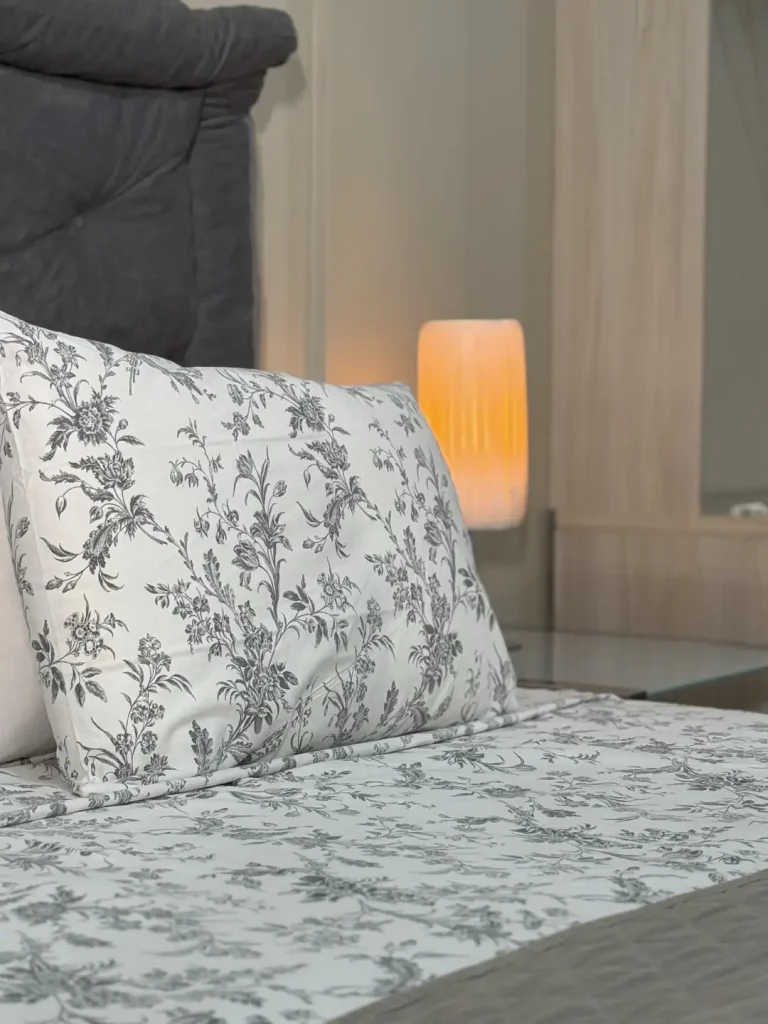 Detalhe do travesseiro e do lençol estampados, com luminária acesa ao fundo