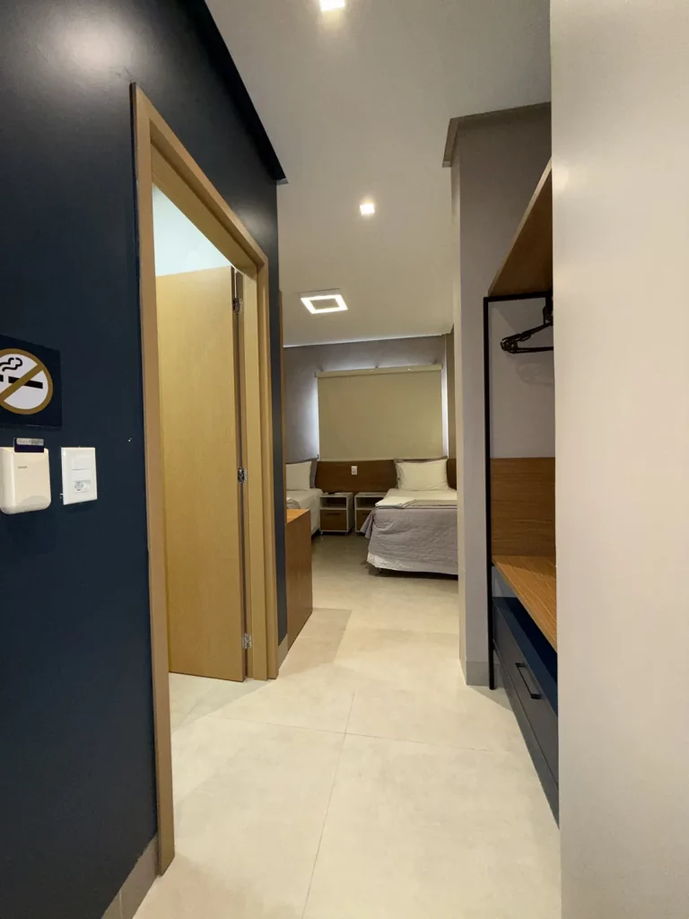 Corredor de entrada com armário aberto e porta do banheiro, com as camas ao fundo