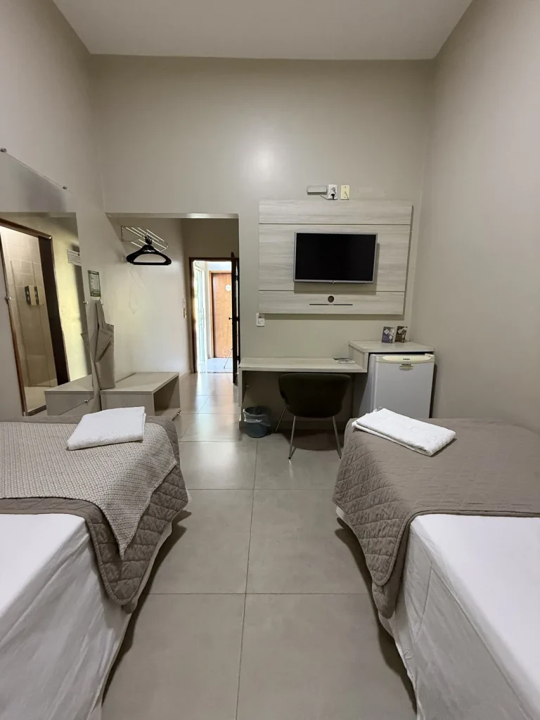 O quarto visto das camas, com espelho, cabideiro, bancada e porta de entrada