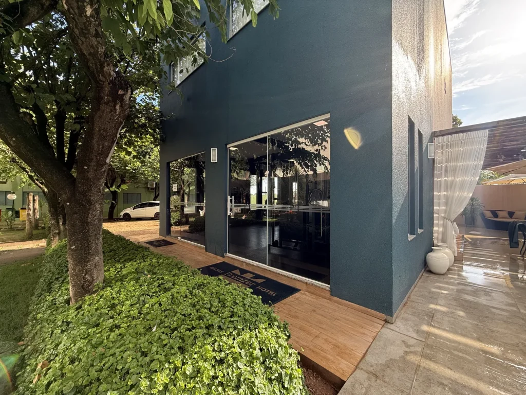 Fachada azul da academia com portas de vidro, caminho de deque e canteiro de arbustos sob as árvores