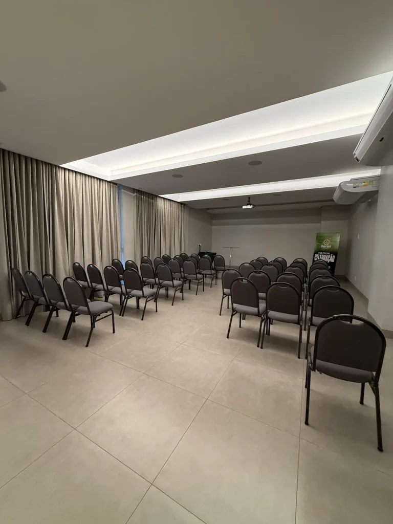 Fileiras de cadeiras estofadas sob a iluminação de sanca do Auditório Premier