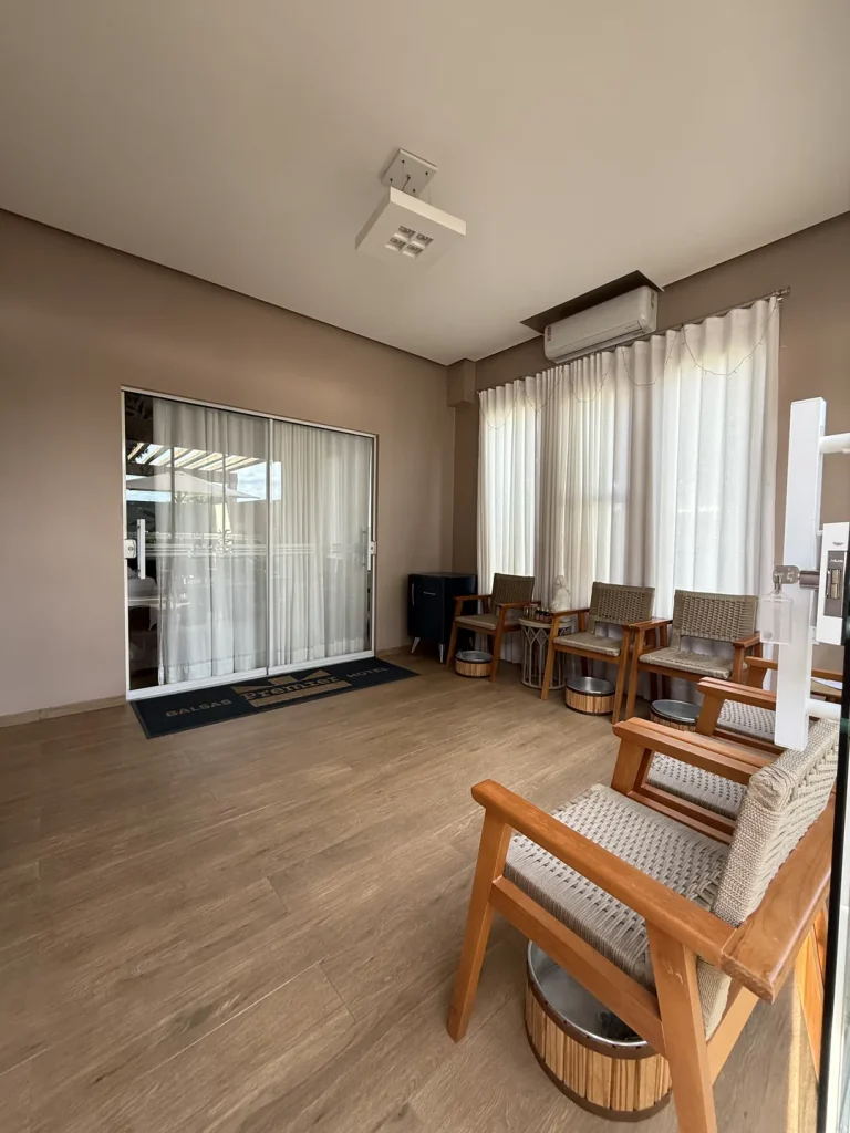 Sala com poltronas de madeira e assento trançado, cada uma com bacia de escalda-pés, cortinas claras e porta de vidro