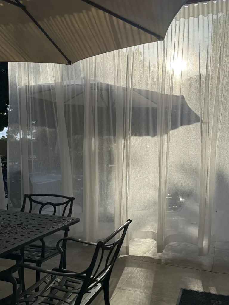 Cortinas translúcidas iluminadas pelo sol, com mesa de ferro em primeiro plano