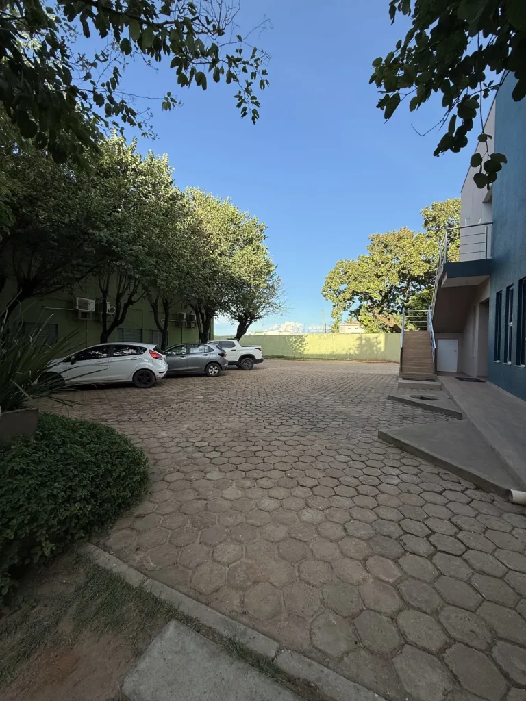 Estacionamento com carros sobre piso intertravado, entre árvores e prédio