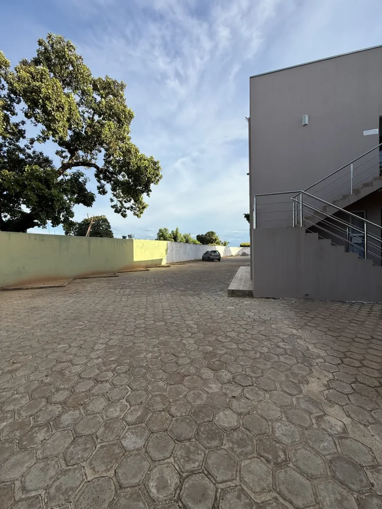Lateral do prédio com escada externa, árvore grande e pátio vazio