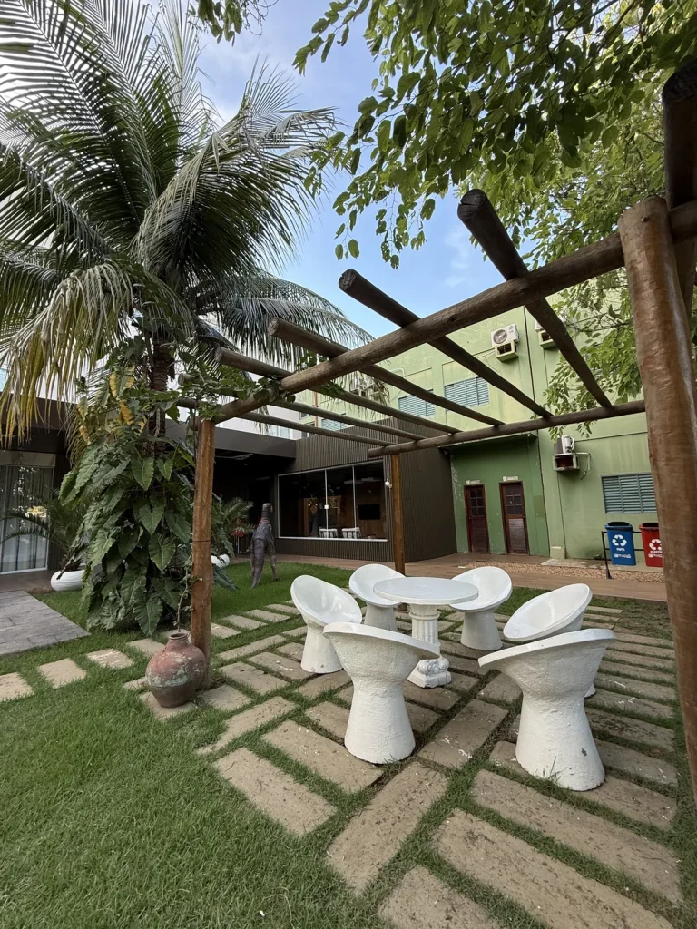 Pergolado de madeira sobre o gramado com poltronas brancas e mesa