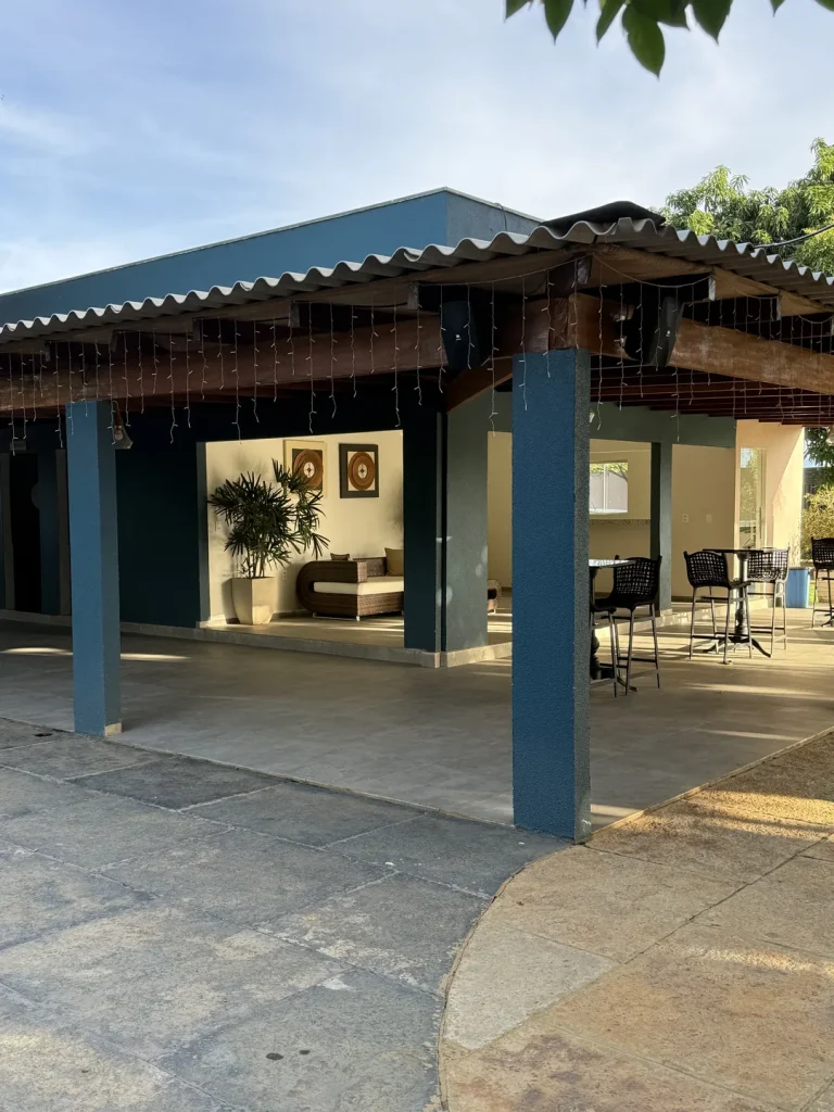 Área coberta com pilares azuis e sala de estar ao fundo