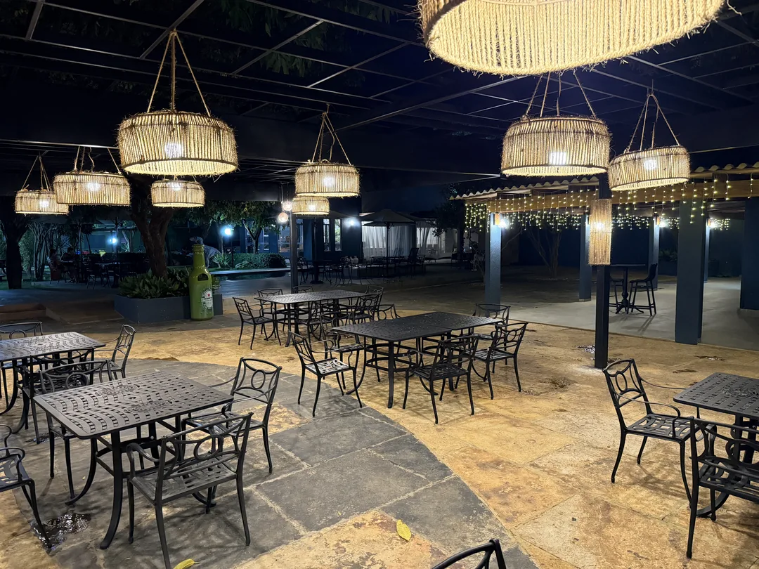 Área de mesas do Jardim Premier à noite, sob luminárias de palha acesas