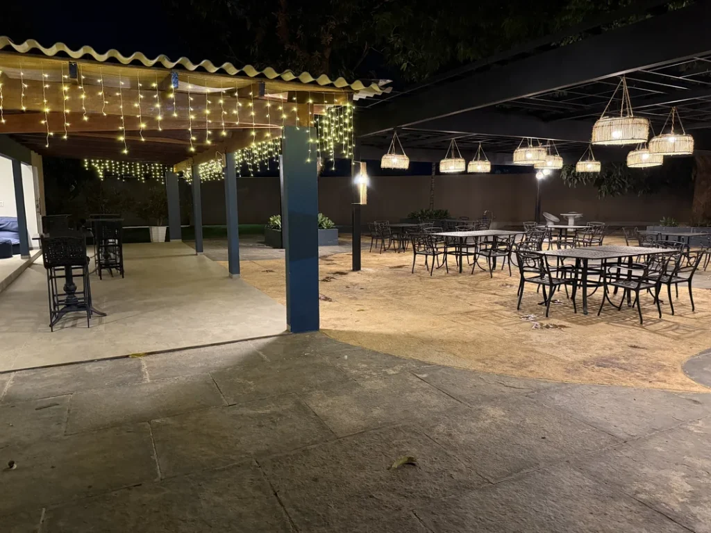 Área coberta à noite com cordão de luzes, luminárias pendentes e mesas